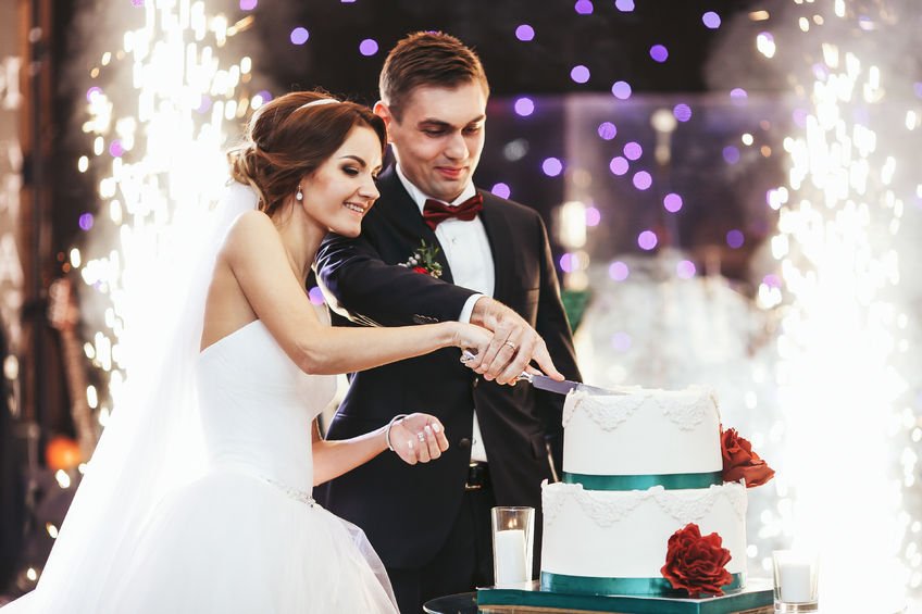64223820 Happy Bride And Groom Cut The Wedding Cake In The Front Of Fireworks